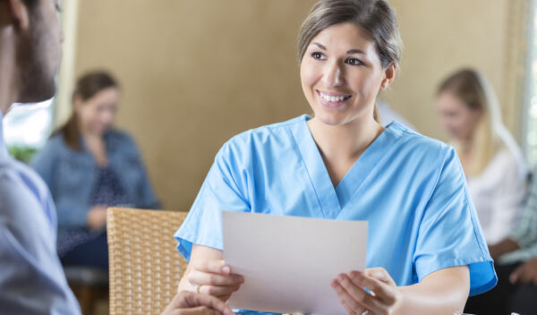 Friendly mid adult Caucasian woman is manager of nursing staff at hospital. She is reading a resume and interviewing a potential  employee. Other candidates are waiting to be interviewed during hospital's healthcare staff recruitment event.
